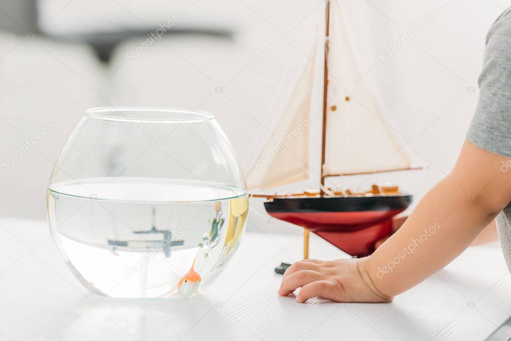 partial view of boy standing near fish bowl and wooden ship model