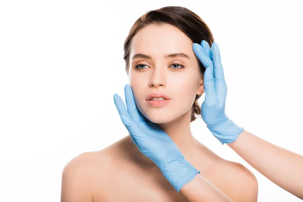 白の上に孤立したブルネットの女性の顔に触れるブルーラテックス手袋におけるプラスチック外科医のクロップドビュー — ストック写真