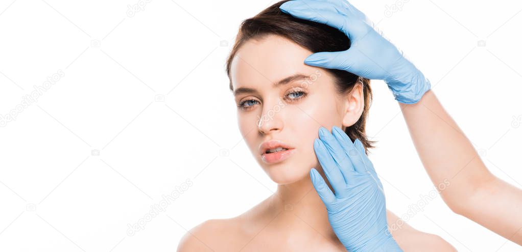 panoramic shot of plastic surgeon in latex gloves touching face of attractive woman isolated on white