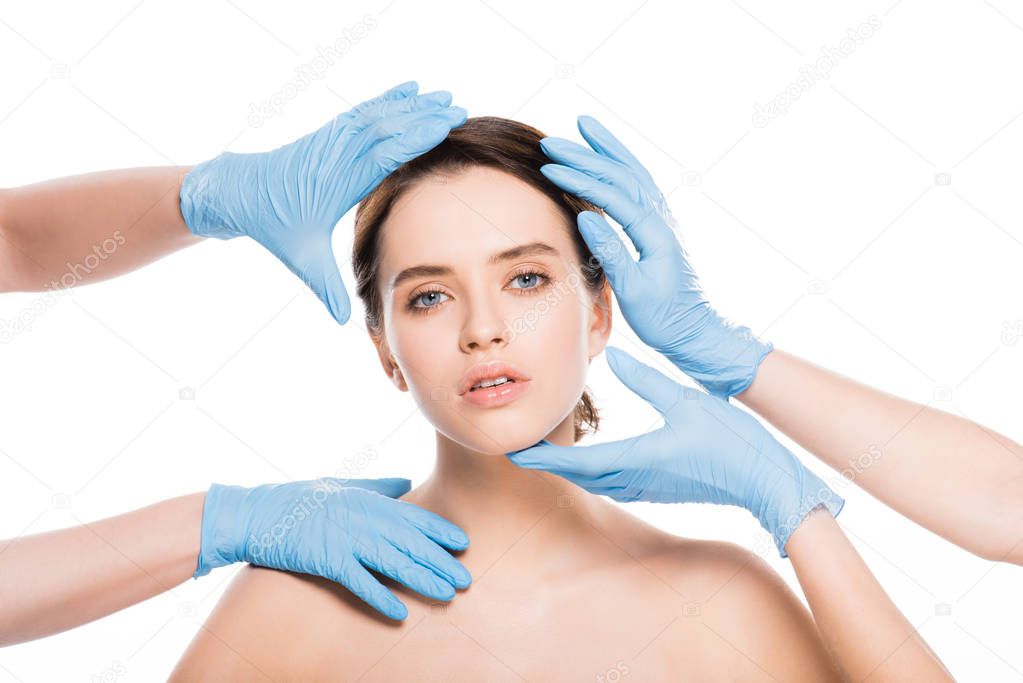 cropped view of plastic surgeons in blue latex gloves touching face of naked girl isolated on white
