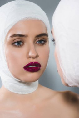 gri üzerinde ayna yakın bandajlı kafa ile genç güzel kadın 