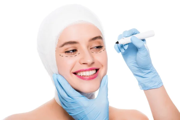 裁剪的意见整形外科医生在乳胶手套拿着标记笔附近的快乐妇女与标记在脸上查出在白色 — 图库照片