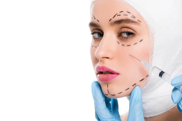 白の上に孤立したマークを持つ女性の顔の近くにシリンジを保持するラテックス手袋中のプラスチック外科医のクロップドビュー — ストック写真