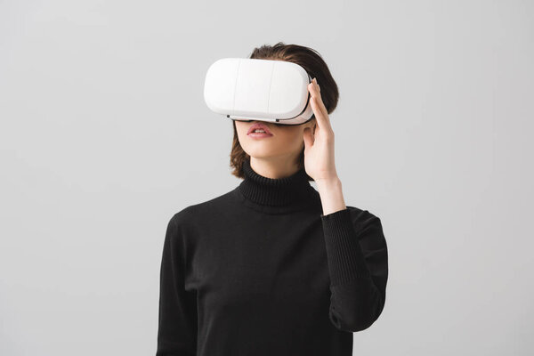 brunette young woman touching virtual reality headset isolated on grey  