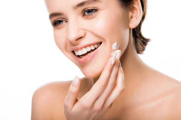 cheerful young brunette woman applying face cream isolated on white 