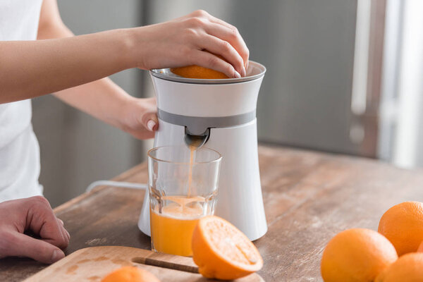 cropped view of woman preparing tasty orange juice in kitchen 