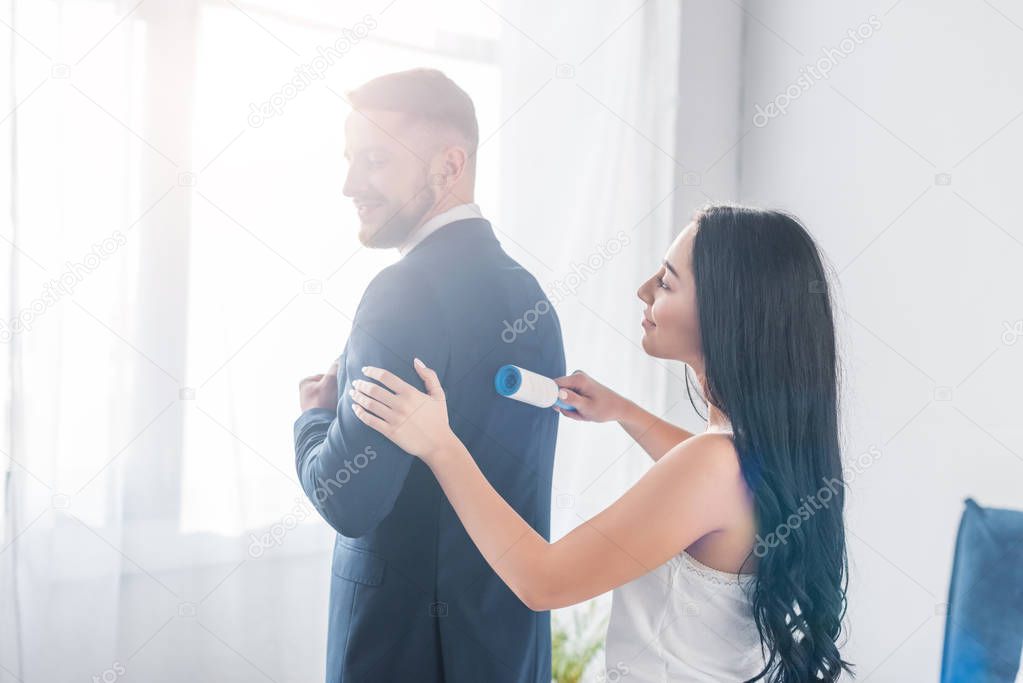 cheerful brunette girl cleaning formal wear of handsome man 