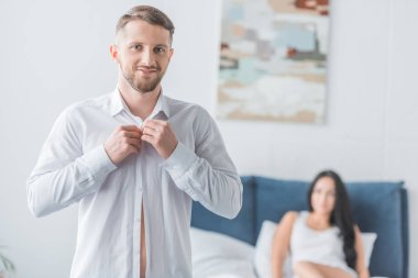 neşeli sakallı adam gömlek giyen ve yatakta kadının yanında kamera bakıyor 