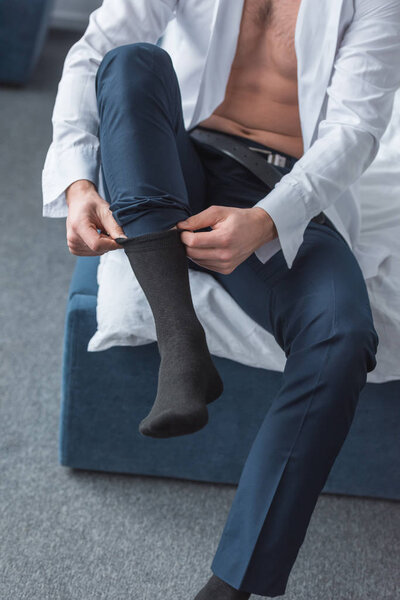 cropped view of man sitting on bed and wearing black socks in bedroom 