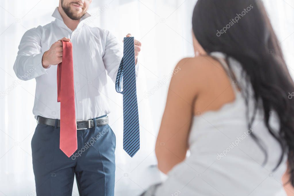 cropped view of cheerful man holding red and blue ties near brunette girl 