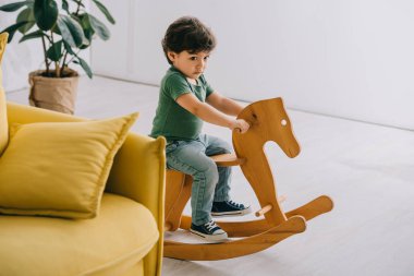 Sevimli küçük çocuk oturma odasında ahşap sallanan at üzerinde oturan