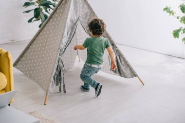 child in jeans running to grey wigwam in living room clipart