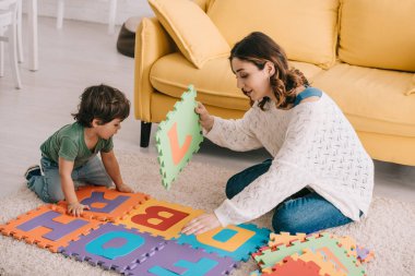 Anne ve oğlu halı üzerinde alfabe bulmaca paspas ile oynuyor