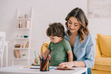 Mother and son drawing with color pencils in living room clipart