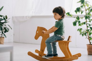 oturma odasında ahşap sallanan at üzerinde oturan çocuk