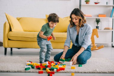 Anne ve oğlu oturma odasında halı üzerinde lego ile oynuyor