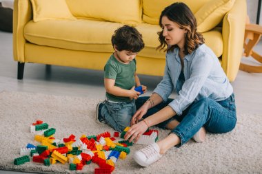 Anne ve oğlu oturma odasında halı üzerinde lego ile oynuyor