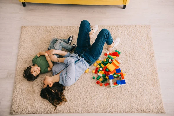 微笑的妈妈和他的儿子躺在地毯上与玩具块的头顶视图 — 图库照片