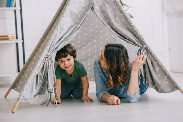 Mom and smiling little son in grey wigwam at home