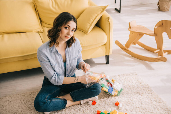 Woman with toy blocks sitting with crossed legs on carpet 