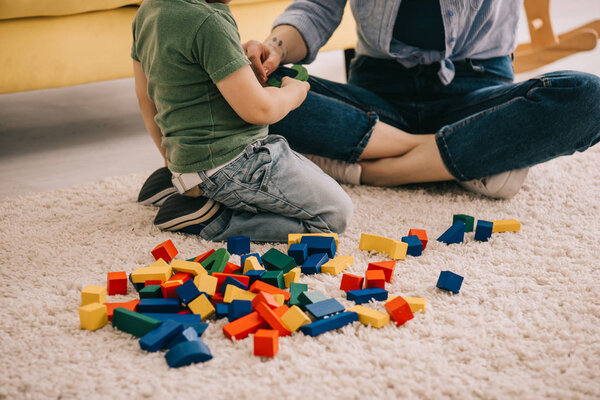 Cropped view of mother and son playing with toy blocks on carpet