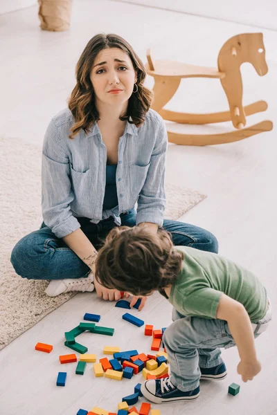 Triste Cansado Mãe Sentado Chão Enquanto Filho Brincando Com Blocos — Fotografia de Stock