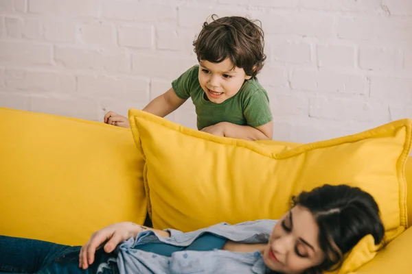 Little Boy Standing Tired Mother Lying Yellow Sofa Living Room — Stock Photo, Image