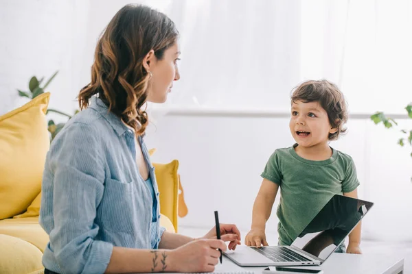 Mujer Mirando Hijo Mientras Trabaja Con Ordenador Portátil Casa — Foto de Stock