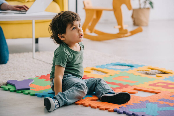 Любопытный парень в джинсах сидит на коврике с буквами
