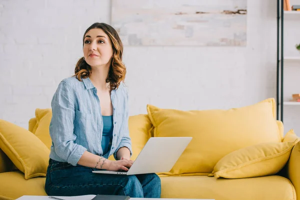 Dromerige Vrouw Zittend Gele Bank Met Laptop Zoek Weg — Stockfoto