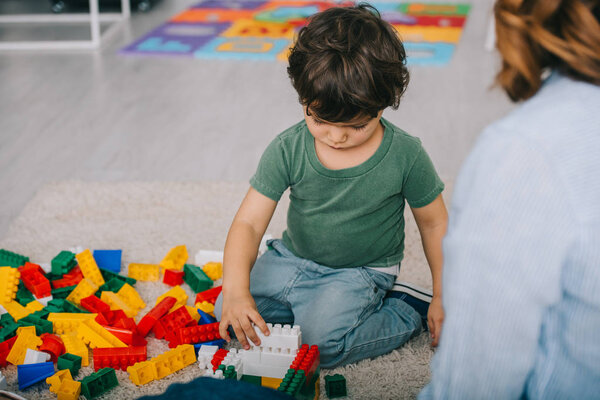 cropped view of mother and son playing with lego on carpet in living room