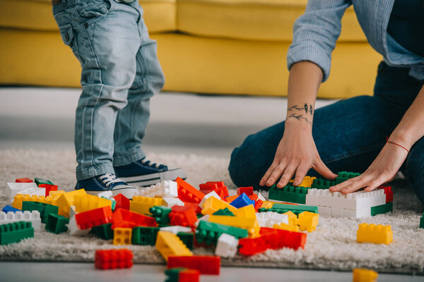 cropped view of mother and son playing with lego on carpet in living room