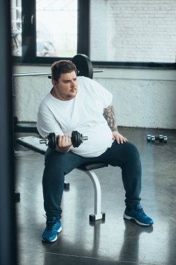 Kilolu dövmeli adam oturma ve spor merkezinde dumbbell ile egzersiz