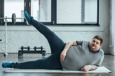 fitness mat ve spor salonunda bacaklar germe yatan kilolu dövmeli adam