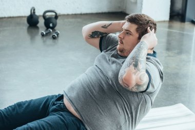 kilolu dövmeli adam spor merkezinde egzersiz kadar oturup yapıyor