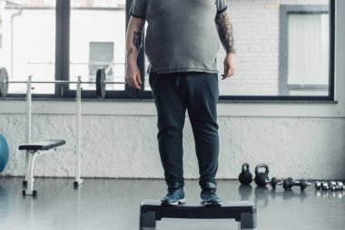 spor merkezinde adım platformu üzerinde duran kilolu dövmeli adam kırpılmış görünümü
