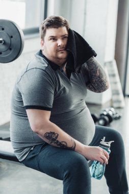 spor şişesi tutan ve spor salonunda havlu ile yüz silme kilolu dövmeli adam