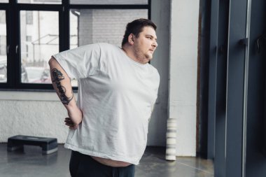 beyaz t-shirt obez dövmeli adam spor merkezinde germe egzersiz yapıyor