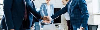 panoramic shot of cheerful businesswomen and multicultural men putting hands together  clipart