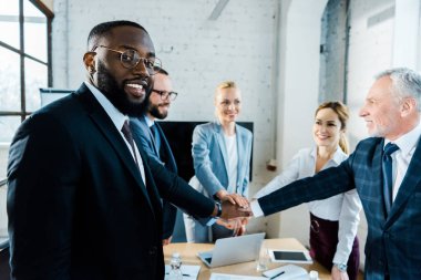 iş arkadaşları ile birlikte el koyarken kameraya bakarak neşeli afrikalı-amerikalı adam 