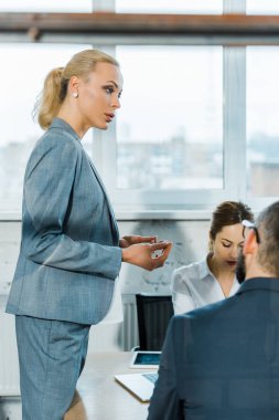 konferans odasında iş arkadaşları nın yanında duran çekici sarışın iş koçu seçici odak 