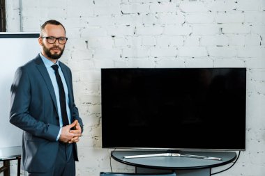 boş ekran ile tv yakınında sıkıştırılmış elleri ile ayakta gözlük yakışıklı sakallı iş koçu 