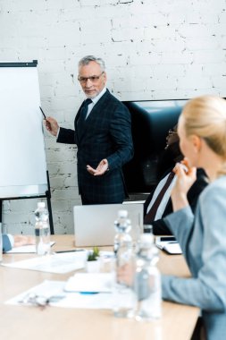 çok kültürlü iş arkadaşları nın yanında kalemle beyaz tahtayı işaret eden iş koçunun seçici odağı 