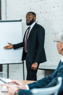 yakışıklı afro-amerikan iş koçu seçici odak konuşma ve beyaz tahta yakınında gesturing 