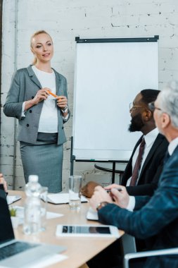 çekici hamile iş koçu seçici odak beyaz tahta yakınında duran ve çok kültürlü iş arkadaşları bakarak 