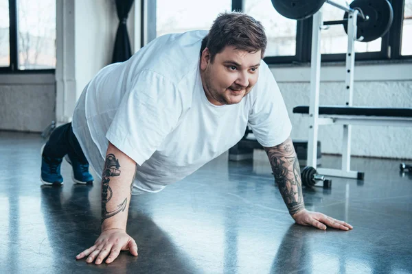 overweight tattooed man doing push up exercise at sports center