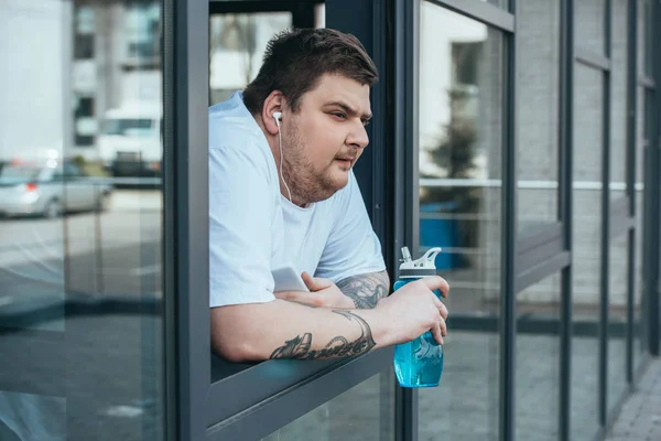 Hombre Con Sobrepeso Con Auriculares Teléfono Inteligente Que Sostiene Botella — Foto de Stock