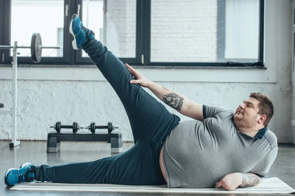 Overweight Tattooed Man Lying Fitness Mat Stretching Legs Gym — Stock Photo, Image