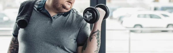 コピースペースを持つジムでダンベルでトレーニング太りすぎの入れ墨の男のパノラマショット — ストック写真
