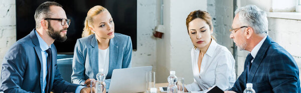 panoramic shot of handsome businessmen in eye glasses sitting near attractive businesswomen 